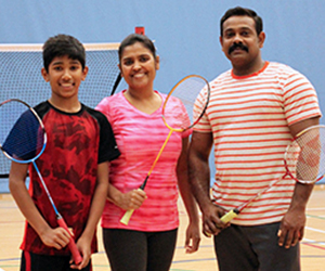 L-R son, mom, dad standing in front of a badminton net, holding badminton racquets