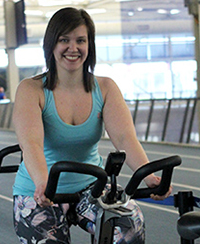Female Spin instructor sitting on a spin bike with the indoor Track in the background