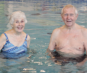 Senior female and senior male stand beside each other in a waist deep swimming pool