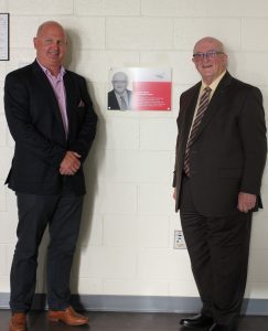 Jeff McKinnon, Canada Games Centre Society Board Chair and Russell Walker smiling in front of plaque