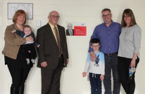 Russell smiling with son, daughter, grandsons and daughter-in-law in front of plaque
